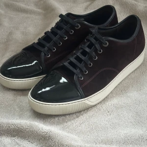 Lanvin sneakers i mörk vinröd mocka - Lanvin sneakers med vinröd mocka och svart lackad tå. Snygga svarta snören och vit platt sula ger en clean look. Insidan är i svart skinn och detaljerna är stilrena. Uk 10 passar 44 eller 44.5