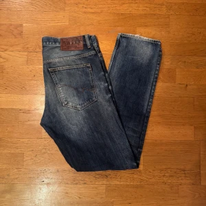 Crocker 319 Carrot jeans blå 32/34 - Snygga blå jeans från Crocker, modell 319 Carrot. De har en klassisk femficksdesign, raka ben och coola slitningar för en avslappnad vibe. Jeansen är gjorda i slitstarkt denim med mörk tvätt och subtila kontrastsömmar. Perfekt för dig som gillar en enkel och stilren look.