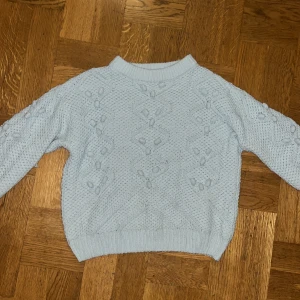 Ljusblå stickad tröja från Zara - Supermysig ljusblå stickad tröja från Zara med snyggt strukturmönster och detaljerade bollar på framsidan och ärmarna. Tröjan har ribbad hals, muddar och nederkant, samt långärmad passform. Perfekt för dig som gillar chill och stilren vibe.