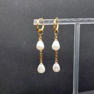 Guldörhängen med droppformade pärlor - Snygga örhängen i guldton med två droppformade vita pärlor som hänger i kedja. Material-rostfritt stål 