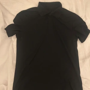 Svart kortärmad skjorta med krage - En stilren svart skjorta med klassisk krage och korta ärmar. Skjortan har en enkel design utan synliga mönster eller detaljer, perfekt för dig som gillar minimalistiskt och cleant. Materialet känns mjukt och bekvämt mot huden.