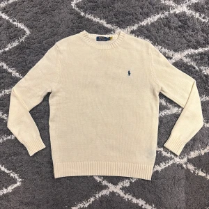 Polo Ralph Lauren tröja Beige  - Snygg beige stickad tröja från Polo Ralph Lauren med klassisk blå broderad logga på bröstet. Rund hals och ribbade muddar vid ärmslut och nederkant. Jag är 180cm, 68kg och den passar mig perfekt.