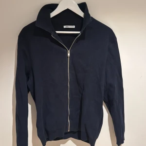 Marinblå zip-kofta från Zara - Snygg marinblå kofta från Zara med hel dragkedja framtill och hög krage. Tröjan har långärmad design och är tillverkad i mjuk bomull, perfekt för lager-på-lager. Enkel och stilren look som funkar till jeans eller chinos.