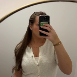 Vit stickad blus med knappar - Mysig vit stickad blus med kort ärm och silvriga knappar framtill. Toppen har en v-ringad design. Använd en gång