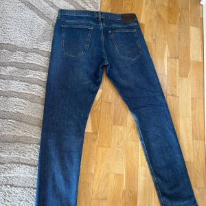 Blå Lee Luke jeans W34 L34 - Säljer ett par klassiska blå Lee Luke jeans med raka ben och snygga kontrastsömmar. Jeansen har två bakfickor, Lee-lapp i läder baktill och är tillverkade i slitstarkt bomullsjeans. Perfekta för dig som gillar en tidlös look.