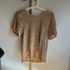 Beige kortärmad blus med struktur - Säljer en beige blus med korta ärmar och snyggt strukturerat tyg. Toppen har en rund halsringning och en lätt loose passform som ger en avslappnad vibe. Perfekt att styla med jeans eller kjol för en trendig look. Storlek L men passar m/s