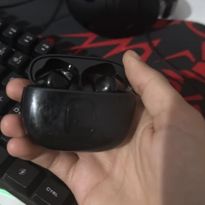 Samsung Galaxy Buds - Svarta Samsung Galaxy Buds i laddningsfodral. Fodralet har synliga repor och slitage, men hörlurarna ser ut att vara i gott skick. Perfekt för trådlös musik och samtal med bra batteritid och bekväm passform.