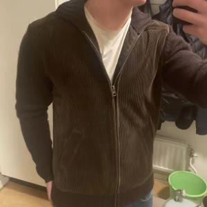 Brun stickad cardigan - Otroligt fin unik stickad cardigan med Manchester på vid magen/framsidan. Ärmarna/ryggen är stickad. Modellen är 180cm, 73kg.