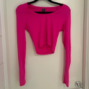 Neon rosa magtröja  - Säljer en croppad långärmad topp från SHEIN i en stark rosa färg. Toppen har en rund halsringning och är figurnära med stretchigt syntetmaterial. Perfekt för dig som gillar färgstarka och trendiga plagg med enkel design.