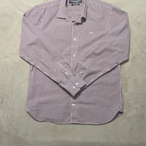 Röd Rutig Swedemount skjorta M - Snygg rutig skjorta från Swedemount i storlek M, med vit och vinröd färg. Skjortan har klassisk krage, långa ärmar och knappar framtill. Materialet är bomull och har easy iron-funktion. Broderad Swedemount logga på bröstet för extra stilpoäng.