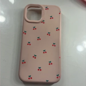 Rosa mobilskal med körsbärsmönster, IPhone 15 - Sött rosa mobilskal med körsbärsmönster, passar iPhone-modeller med stor kameramodul. Skalet är i gott skick med minimalt slitage, mjukt material som ger bra skydd och grepp. Perfekt för dig som vill ge din mobil en personlig och lekfull touch.