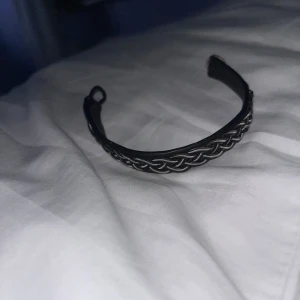 Svart och silver samiskt armband - Unikt samiskt armband med flätad tenntråd i silverfärg på svart skinn. Armbandet har en snygg knäppning med knapp i ben och den klassiska flätade designen som ger en cool och tidlös vibe. Perfekt för dig som gillar detaljer och nordisk stil.