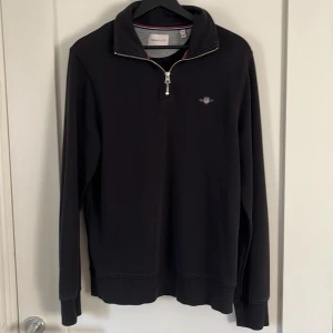 Svart half zip tröja från GANT - Svart långärmad tröja från GANT med half zip vilket är trendigt och snyggt. Tröjan har broderad logga på bröstet och snygga detaljer i rött och blått på insidan av kragen. Perfekt för dig som gillar stilrena och klassiska plagg. Inprinsip aldrig använd. Kom gärna med frågor m.m //Vilmer