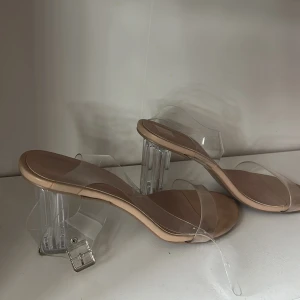 Beige sandaler med transparent klack - Säljer ett par sandaler i beige med transparenta remmar och coola klara blockklackar. Remmarna är i syntet och har ett silvrigt spänne. Snyggt minimalistiskt utseende med rund tå och platt sula framtill. Perfekt för dig som gillar statement-klackar. Klackarna användes några gånger förra sommaren men slutade fort för de var för stora för mig‼️ dom är skön och jag ser inga problem med användningen av dom förutom de passar inte längre mig. 🥰