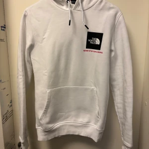 Vit hoodie från The North Face XS - Säljer en clean vit hoodie från The North Face i storlek XS. Tröjan har huva med snörning, stor magficka och svart logga på bröstet samt ryggen. Tillverkad i mjuk bomullsmix, perfekt för chill eller streetwear.