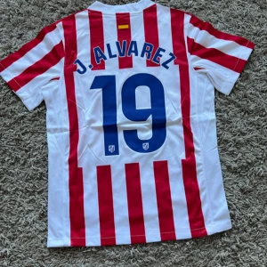 Atletico Madrid J. Alvarez 19 Nike tröja small - Säljer en officiell Atletico Madrid fotbollströja från Nike med J. Alvarez och nummer 19 på ryggen. Tröjan är kortärmad, har röda och vita vertikala ränder, klubbmärke på bröstet och sponsortryck. Tillverkad i lätt Dri-FIT material som andas.
