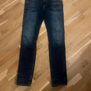 Replay anbass mörkblå jeans - Snygga Replay Hyperflex jeans i mörkblå tvätt med klassiska fem fickor och coola detaljer på bakfickorna. Stretchigt material för extra komfort och slim passform. Perfekt för dig som gillar stilrena och moderna jeans.