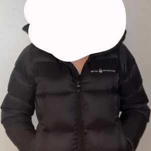 Svart dunjacka från Sail Racing - Svart dunjacka från Sail Racing med huva och dragkedja framtill. Jackan har en puffad design och logga på bröstet. Perfekt för kalla dagar ! Jag har aldrig haft en sån bra vinter jacka innan,Säljer denna då jag ska köpa en ny modell hade den några vinter dagar förra vintern och ingen jacka har hållt mig så varm som denna , Ingen skada ,inget lukt,helt fläckfri jacka , Tvättas innan den skickas iväg såklart!! Hör gärna av er om ni är intresserade 💞