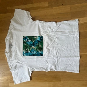 Vit Kenzo t-shirt med tryck - Säljer en vit t-shirt från Kenzo i storlek S. Framsidan har ett fyrkantigt tryck med gröna och blå toner i ett abstrakt mönster. T-shirten är klassiskt kortärmad och gjord i mjuk bomull. Perfekt för dig som gillar streetwear och snygga prints.