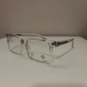 Chrome Hearts klara glasögon - Säljer ett par stilrena glasögon från Chrome Hearts med transparent båge och rektangulär form. Sidorna har snygga silverdetaljer och små dekorationer som ger en lyxig känsla. Perfekta för dig som vill sticka ut med en unik accessoar. Har gold också