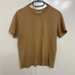 Beige t-shirt från Weekday i bomull - En basic beige t-shirt från Weekday i mjuk bomull. Modellen är klassisk med rund halsringning och korta ärmar. Perfekt för en clean och enkel stil, lätt att matcha med allt. Snyggt avslappnad passform.