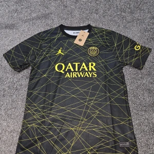 PSG x Jordan svart matchtröja - Svart PSG fotbollströja från Jordan med gula detaljer och grafiskt mönster av tunna linjer. Tröjan har korta ärmar, rund hals och är tillverkad i lätt, ventilerande funktionsmaterial. Stort Qatar Airways-tryck på bröstet och PSG-emblem.