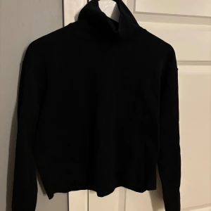 Svart polotröja från Zara - Svart polotröja med lång ärm och hög krage. Tröjan är enkel och stilren, tillverkad i mjuk bomull som känns skön mot huden. Passformen är normal och modellen är klassisk, perfekt för dig som gillar minimalistisk stil.