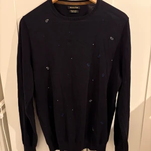 Mörkblå tröja från Massimo Dutti - Snygg mörkblå tröja från Massimo Dutti i extrafin bomull. Tröjan har diskreta små broderade detaljer i blått och vitt samt rund halsringning och långa ärmar. Perfekt för dig som gillar stilrena plagg.