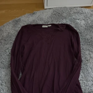 Mörklila långärmad topp från Gina Tricot - Säljer en mörklila långärmad topp från Gina Tricot med v-ringning och spetsdetalj vid halsen. Perfekt för dig som gillar stilrena plagg med en twist. Skön och mjuk känsla, passar till många outfits.
