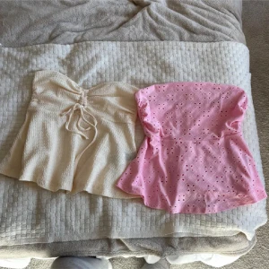 Bandeau toppar  - Säljer två bandeau tubtoppar – en ljusbeige med struktur och snörning framtill, samt en ljusrosa med broderade hål och blommig känsla. Båda är utsvängda nertill och perfekta för sommarens varma dagar. Supersöta att styla med jeans eller kjol! Den är jättefin, men bara den rosa är använd en gång. Man kan välja att köpa en eller båda. Priset är för båda men köper man bara en så kostar den 20.