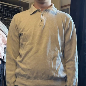 Beige pikétröja med lång ärm - Säljer en stilren beige pikétröja med lång ärm och klassisk krage. Tröjan har tre knappar framtill och ribbad mudd vid midjan och ärmslut. Perfekt för dig som gillar enkel och clean look. Passar dig som vill ha en basic tröja med lite extra stil.