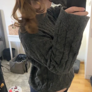 Mörkgrå stickad tröja från H&M - Mysig mörkgrå stickad tröja från H&M i storlek XS. Tröjan har ett snyggt kabelstickat mönster, ribbade muddar och en rund hals. Perfekt för kyliga dagar och passar dig som gillar en loose fit och oversized känsla.