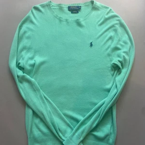 Grön tröja från Polo Ralph Lauren - Grön långärmad tröja från Polo Ralph Lauren i slim fit. Tröjan är tillverkad av mjuk pima bomull och har en klassisk rund hals samt den ikoniska broderade loggan i blått på bröstet. Perfekt för dig som gillar stilrena och fräscha färger.