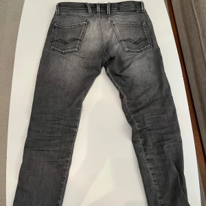 Replay Anbass Slim Fit grå jeans 30/32 - Snygga Replay Anbass jeans i slim fit (30/32) med cool grå tvätt och klassiska fem fickor. Jeansen har svarta och grå toner, diskreta slitningar och detaljerade sömmar på bakfickorna. Perfekt passform för dig som gillar smalare jeans. Skick 7/10, några defekter som ni ser på bilderna men fortfarande mycket kvar att ge