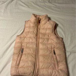 Mer rosa i verkligheten! Ljusrosa dunväst från Five Seasons - Säljer en ljusrosa dunväst från Five Seasons i storlek 130. Västen har quiltad design, hög krage och två fickor med dragkedja. Perfekt för lager-på-lager och har en snygg, enkel look med diskreta detaljer. Dragkedja framtill för smidig användning.