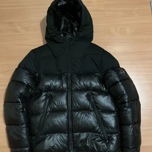 Svart pufferjacka från Replay - Säljer en svart pufferjacka från Replay med stor huva och feta Replay-tryck på insidan och baksidan av huvan. Jackan har två snedställda fickor med dragkedja och en riktigt puffig look. Perfekt för kalla dagar när du vill se chill ut. Pris kan diskuteras vid snabb och smidig affär😊😊