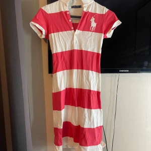 Randig långklänning från Ralph Lauren - Säljer en långklänning från Ralph Lauren i storlek XS med breda röda och vita ränder. Klänningen har korta ärmar, krage och knappar framtill. Ikonisk broderad logga på bröstet. Tillverkad i mjuk bomull, perfekt för en chill och sportig look.