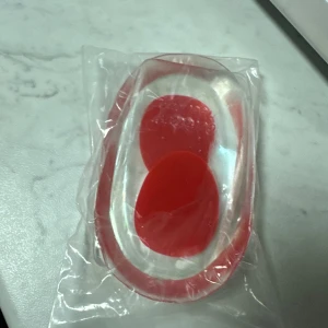 Röda och genomskinliga gel-hälkuddar för skor - Ett par genomskinliga och röda gel-hälkuddar som ger extra komfort och stöd i dina skor. Perfekta att lägga i sneakers eller andra skor för att dämpa stegen och minska belastningen på hälarna. Gjorda i mjukt syntetmaterial.Genom att använda ett mjukt och stötdämpande hälinlägg avlastar du hälsporren direkt. 