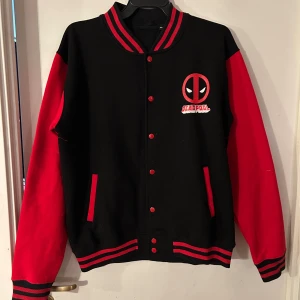 Jacka från Dead pool storlek XL - Helt ny jacka från Desd pool. Storlek XL. Material i 80% bomull. Tror det är en collegejacka. Lite stretchig.