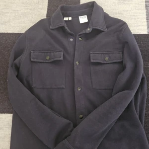 Mörkblå overshirt från Selected Homme - Snygg mörkblå overshirt från Selected Homme med klassisk krage, två bröstfickor med knappar och raka ärmar. Perfekt lager-på-lager-plagg med stilren look och sköna material. Passar till jeans eller chinos för en clean outfit.