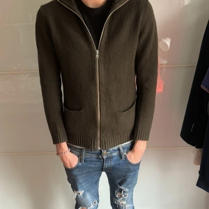 Filippa K stickad tröja - Säljer en mörkgrön stickad kofta med hel dragkedja framtill och två fickor. Koftan har ribbade muddar vid ärmslut och nederkant, perfekt för kyligare dagar. Enkel och stilren design som passar till det mesta. Skriv för frågor!