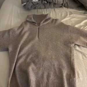 Beige stickad tröja med half zip - Mysig beige stickad tröja med ribbad hög krage och half zip-dragkedja. Tröjan har långa ärmar och bred ribbad mudd nedtill, perfekt för lager-på-lager under kyliga dagar. Den är oversized