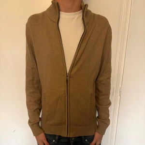 Beige kofta med dragkedja Dressmann - Säljer en beige stickad kofta från Dressmann i storlek S. Koftan har ribbad krage, hel dragkedja framtill och två fickor. Stilig och perekt till hösten. Hör av er vid minsta fundering!