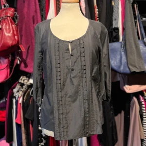 Grå blus från Stockh LM med knappar - Snygg grå blus från Stockh LM med tre dekorativa knappar framtill och diskreta veckade detaljer längs bröstet. Blusen har rund halsringning och trekvartsärmar med lätt puff vid ärmslut. Materialet känns lätt och har en fin lyster.