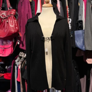 Svart ribbad kofta från Cecil - Svart ribbstickad kofta från Cecil i storlek XL/L. Koftan har en snygg krage och stängs framtill med två metallspännen. Långärmad och i mjukt stickat material.