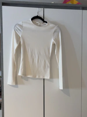 Vit ribbad långärmad topp H&M XS - Använd 1 gång. Säljer en stilren vit långärmad topp från H&M i storlek XS. Toppen har en ribbad struktur och är figurnära med rund hals. Perfekt att matcha med jeans eller kjol för en clean look.