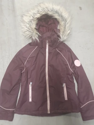 Vinterjacka - Vinterjacka i vinröd lila färg från H&M med huva och fuskpäls. Jackan har ljusa detaljer, dragkedjor framtill och två fickor. På ärmen sitter ett rosa badge med texten 'Support Your Local Girl Crew'. Perfekt för kalla dagar och har en snygg, sportig vibe.