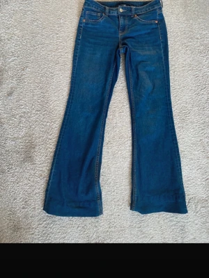 Blå bootcut jeans från H&M Divided - Snygga blå jeans från H&M Divided i storlek 38 men passar även S som jag vanligtvis brukar bära. Modellen har klassisk femficksdesign, låg midja och bootcut-ben som ger en schysst siluett. Jeansen är tillverkade i jeansmaterial med kontrastsömmar och knappstängning framtill. Bara använda en gång!!!
