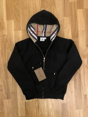 Svart Burberry zip-up - En snygg zip-up från Burberry i svart. Den har storlek M, men passar S på grund av att armarna är lite kortare. Den skulle passa någon i storlek S/XS perfekt!