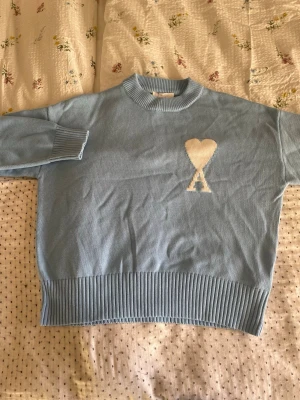 Ljusblå stickad tröja från Ami Paris - Säljer nu en av årets julklappar: en ami Paris tröja. Tröjan satt lite stort på mig(som ses på bilden) och gick ej att returnera, därav säljes.                            Tröjan är helt oanvänd och alltså i perfekt skick.                                                 Vid minsta fråga är det bara höra av sig, mvh 